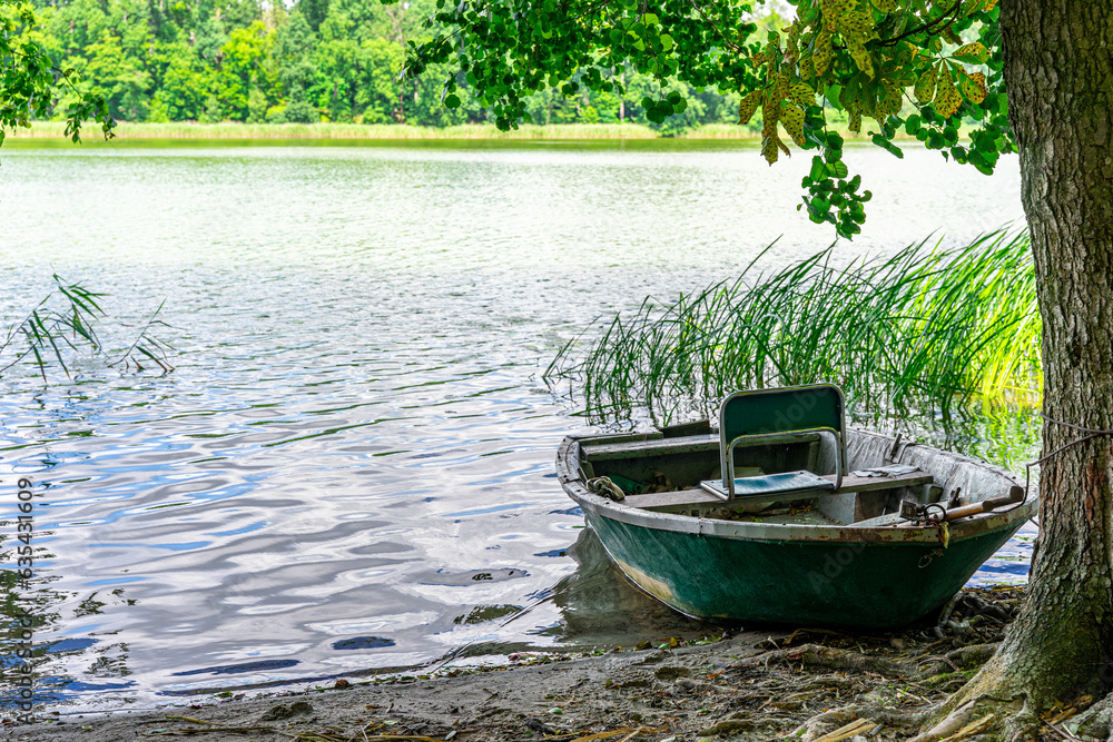The rowing fishing boat in the foreground moored under a chestnut tree on the shore. The rowing fishing boat in the foreground moored under a chestnut tree on the shore.