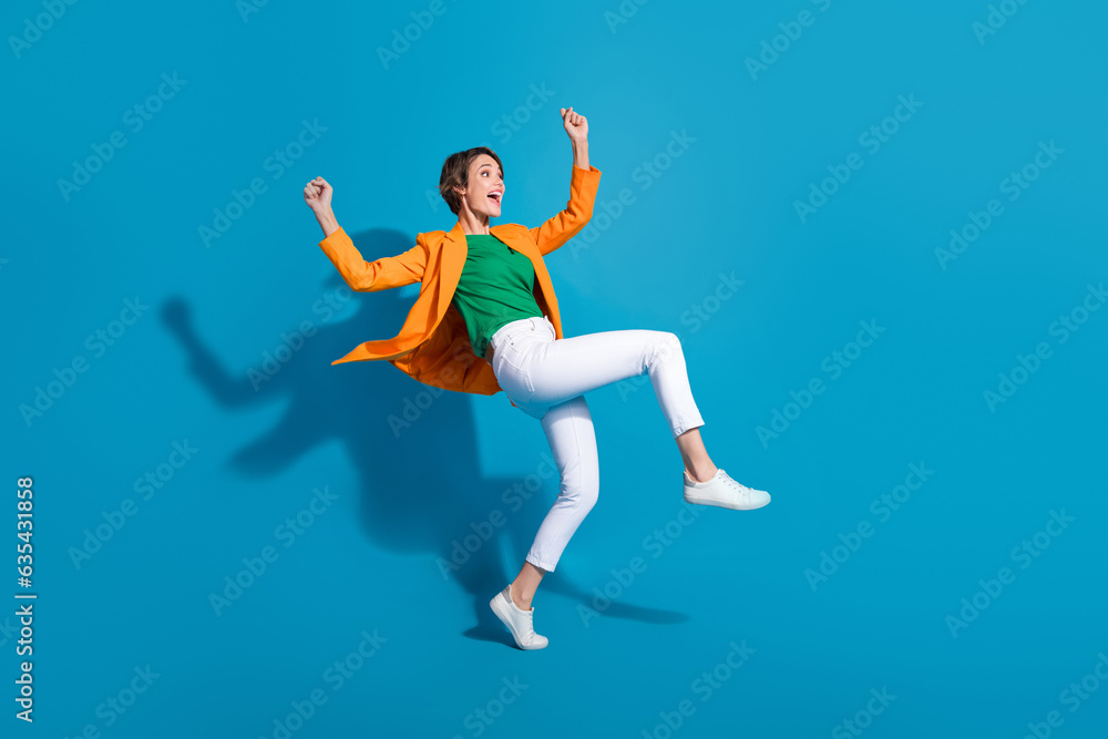 Profile side full length photo of carefree crazy funky lady wear trendy orange clothes celebrate victory isolated on blue color background