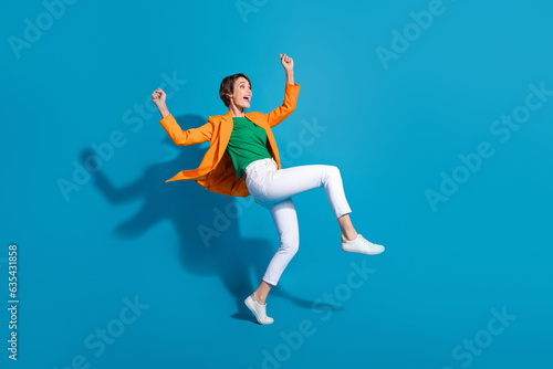 Profile side full length photo of carefree crazy funky lady wear trendy orange clothes celebrate victory isolated on blue color background