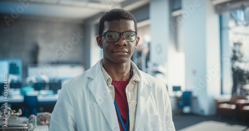 Portrait of Young Handsome Black Man Wearing Glasses and a Lab Coat Looking at the Camera. Future Engineer Pursuing Scientific Career. Industrial Manufacturing Student in University Laboratory Posing © Gorodenkoff