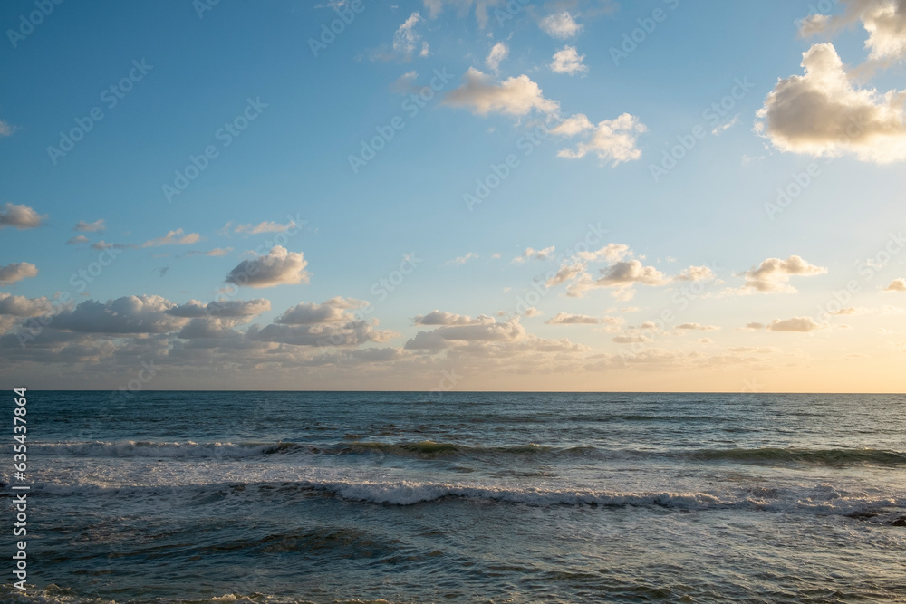 Fototapeta premium Beautiful seascape of cloudy sky lit by dimming sunset light over the calm sea. Ocean view with horizon, background with a lot of copy space for text.