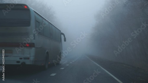 A bus with its headlights on is driving in the fog along on an asphalt road