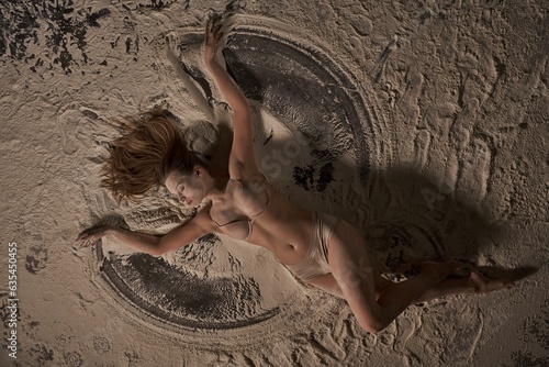 Sexy nude woman lying on a sand with raised hands like a butterfly