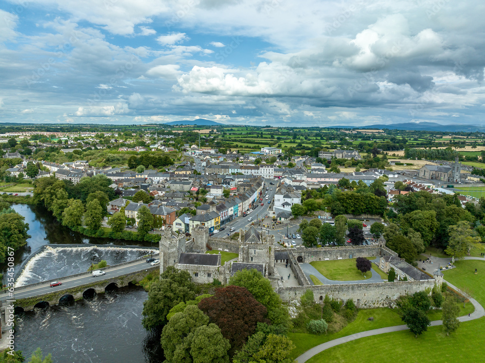 Aerial view of Cahir castle and town in Ireland with Tower House, outer castle, circular, rectangular towers, banquette hall, guarding the crossing on the River Suir with a waterfall and golf course