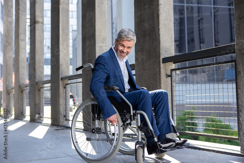 Gray haired disabled man wearing official style suit in wheelchair city background. © zinkevych