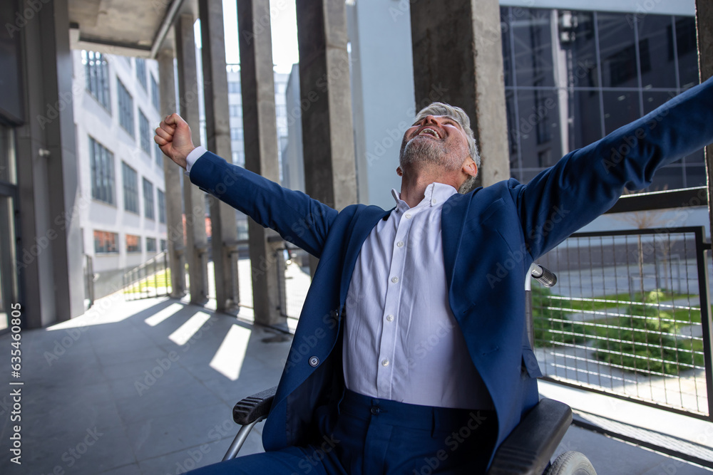 Happy gray haired disabled man wearing suit in wheelchair, raised arms, celebrating his success. Happy gray haired disabled man wearing suit in wheelchair, raised arms, celebrating his success.
