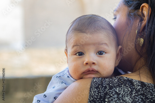 Young Latina mom sitting in a park, holding her newborn baby