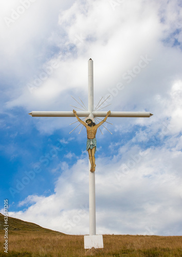 A close-up of a metal cross with Jesus crucified on a hillside against a sky background © sebi_2569