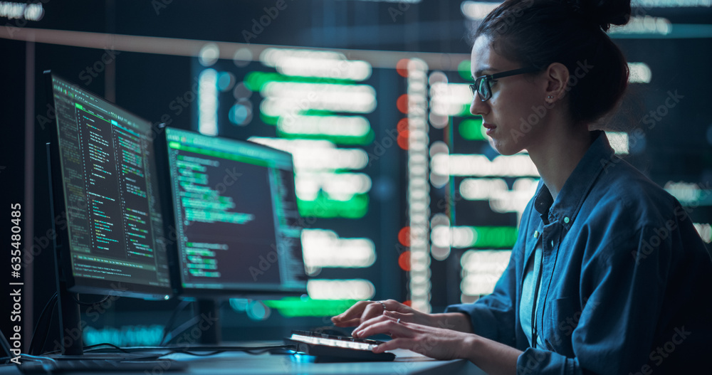 Medium Shot of a Woman Working as a Developer, Surrounded by Big Screens Displaying Lines of Code in a Monitoring Room. Female Programmer Using Desktop Computer, Analysing Data, Creating AI Software Medium Shot of a Woman Working as a Developer, Surrounded by Big Screens Displaying Lines of Code in a Monitoring Room. Female Programmer Using Desktop Computer, Analysing Data, Creating AI Software