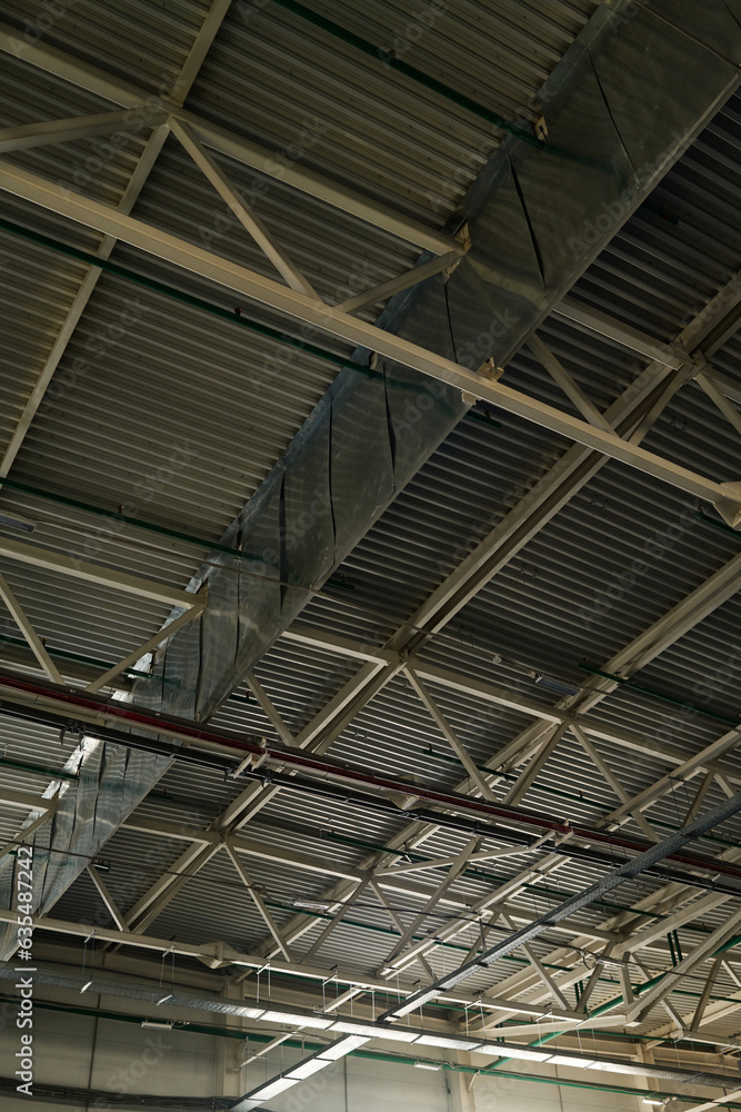Part of ceiling of spacious warehouse or storage room of modern industrial plant or factory represented by metallic structures of grey color Part of ceiling of spacious warehouse or storage room of modern industrial plant or factory represented by metallic structures of grey color