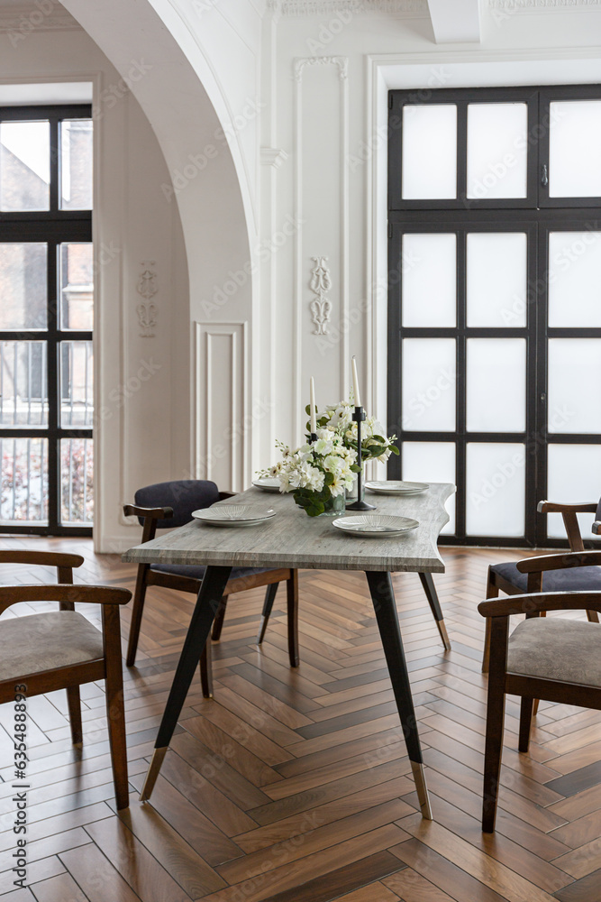 Fototapeta premium a view of a set dining table in a chic expensive bright interior of a huge living room in a historic mansion with arched arches, columns and white walls decorated with ornaments and stucco.