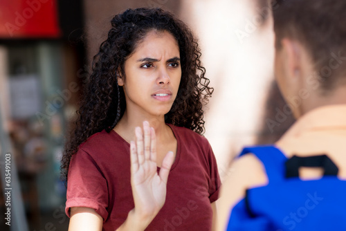 Latin american woman gesturing stop and rejecting young adult man