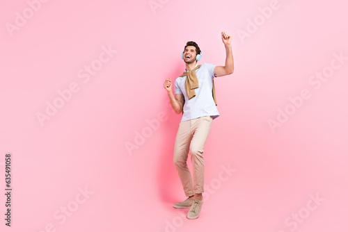 Full size portrait of satisfied glad young man dancing listen music headphones empty space isolated on pink color background
