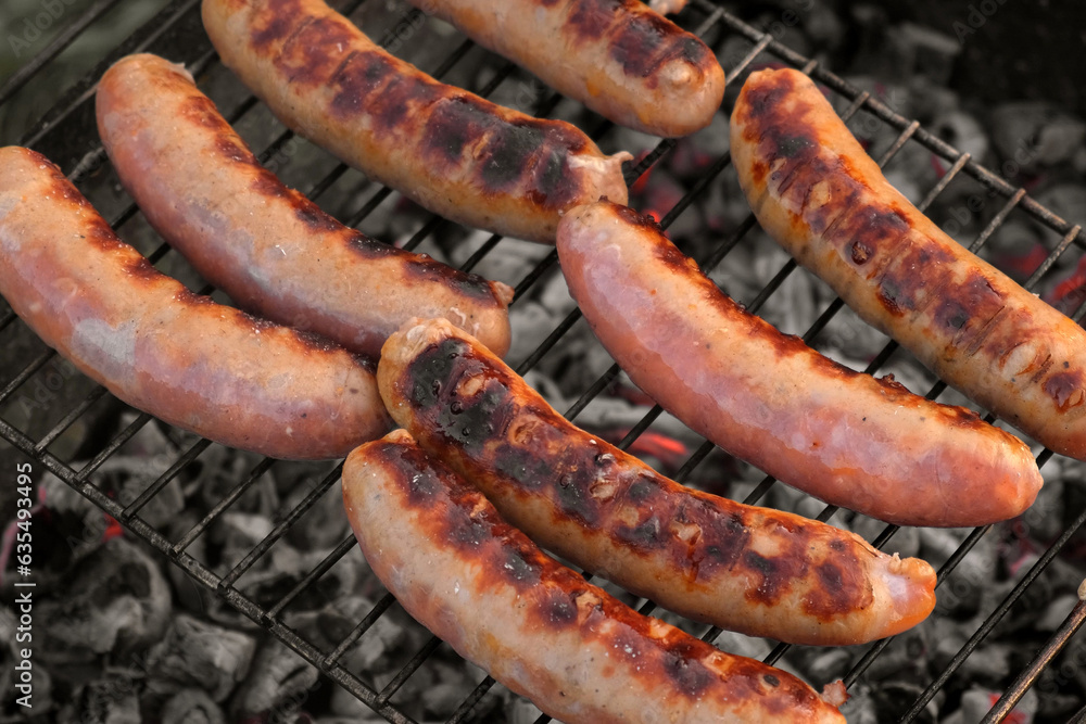 Grilled sausages. Cook man preparing grilling food bbq. Barbecue with smoke, flame outdoors. Tasty juicy german bratwurst. Charcoal kettle grill outside in backyard. Family summer vacation. Close-up	
