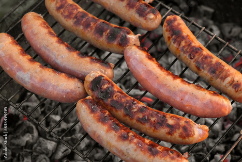 Grilled sausages. Cook man preparing grilling food bbq. Barbecue with smoke, flame outdoors. Tasty juicy german bratwurst. Charcoal kettle grill outside in backyard. Family summer vacation. Close-up	
