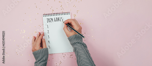 New Year goals 2024. Woman's hand writing in notebook goals list. Concept of new year planning. Banner for web site, design. Flat lay, top view