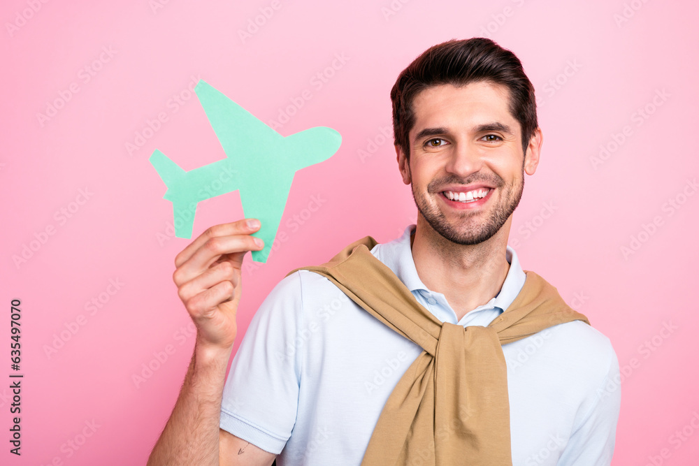 Photo of positive nice man beaming smile arm hold little paper plane tied shoulders sweater isolated on pink color background Photo of positive nice man beaming smile arm hold little paper plane tied shoulders sweater isolated on pink color background