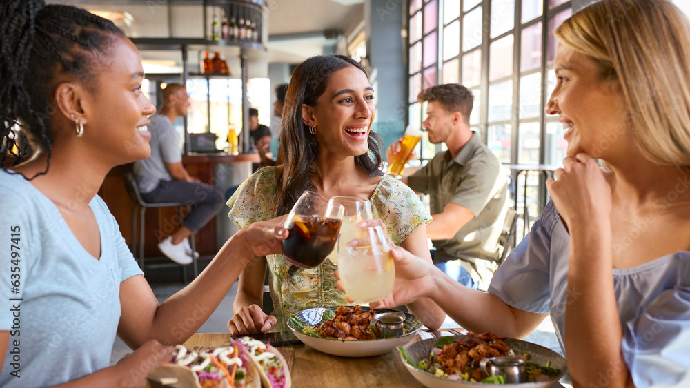 Group Of Female Friends Meeting Up In Restaurant Eating Food And Doing Cheers With Meal Group Of Female Friends Meeting Up In Restaurant Eating Food And Doing Cheers With Meal