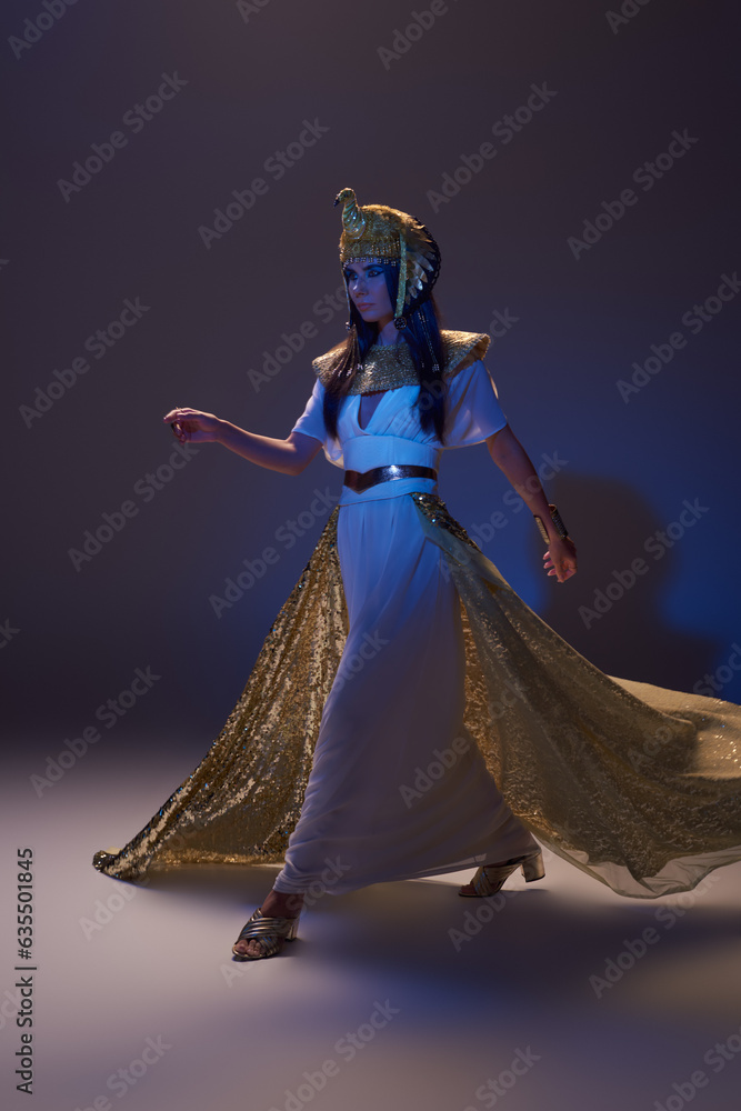 Full length of woman in egyptian look and headdress walking on brown background with blue light Full length of woman in egyptian look and headdress walking on brown background with blue light