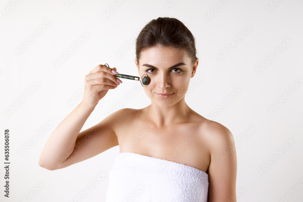 Young woman doing face massage with roller against white studio background. Anti-wrinkles. Refreshment. Concept of female beauty, skin care, cosmetology and cosmetics, health, ad Young woman doing face massage with roller against white studio background. Anti-wrinkles. Refreshment. Concept of female beauty, skin care, cosmetology and cosmetics, health, ad