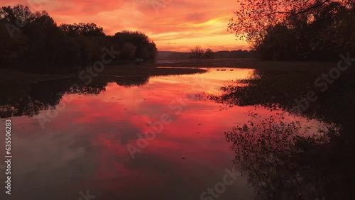 Mirror reflection of beautiful sunset over still lake with birds and distant interstate travel bridge 