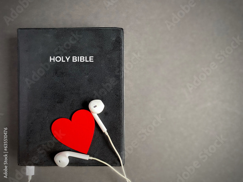 Earphones with red heart on the Bible. Symbolises devotion and love for hearing God's words. Christianity concept.