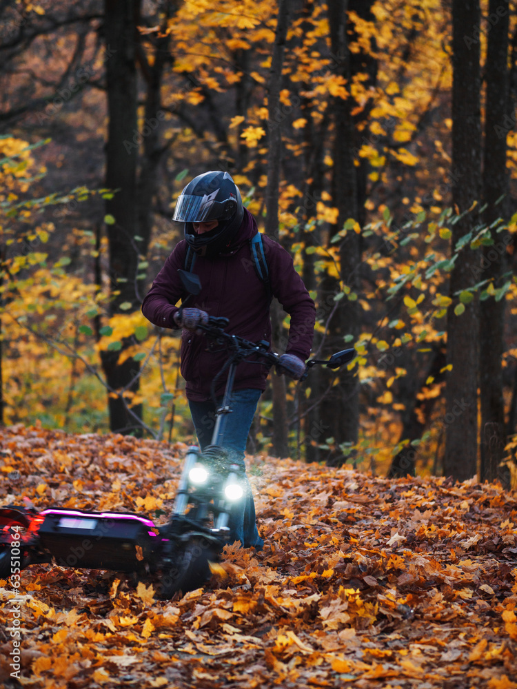 A man in a helmet rides through a colorful autumn forest on a powerful electric scooter A man in a helmet rides through a colorful autumn forest on a powerful electric scooter
