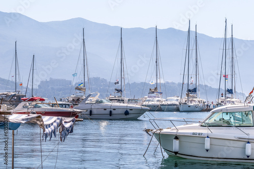 Budva, Montenegro - June 17, 2021: A row of yacht masts against the backdrop of foggy mountains in the port of Dukley Marina in Budva. Personal boats on the surface of blue shiny water in the morning