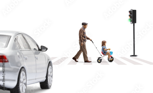 Full length profile shot of an elderly man walking and pushing a girl on a tricycle a street