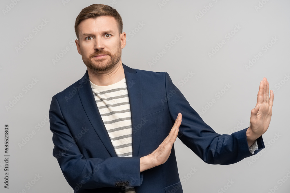 Fototapeta premium Frustrated man with disgust on serious face incredulously pushes away troubles with gesture of hands isolated on gray background. Male with angry expression refuse something bad showing denial.