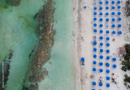 Drone aerial of tropical sandy beach holiday resort with beach umbrellas and people swimming and relaxing. Summer vacations.