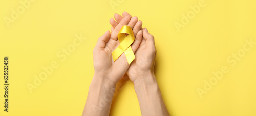 Foto Hands with golden awareness ribbon on yellow background