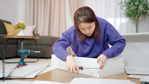 Young asian women using tightens screw for assembling new furniture by herself at home. Assembling furniture concept