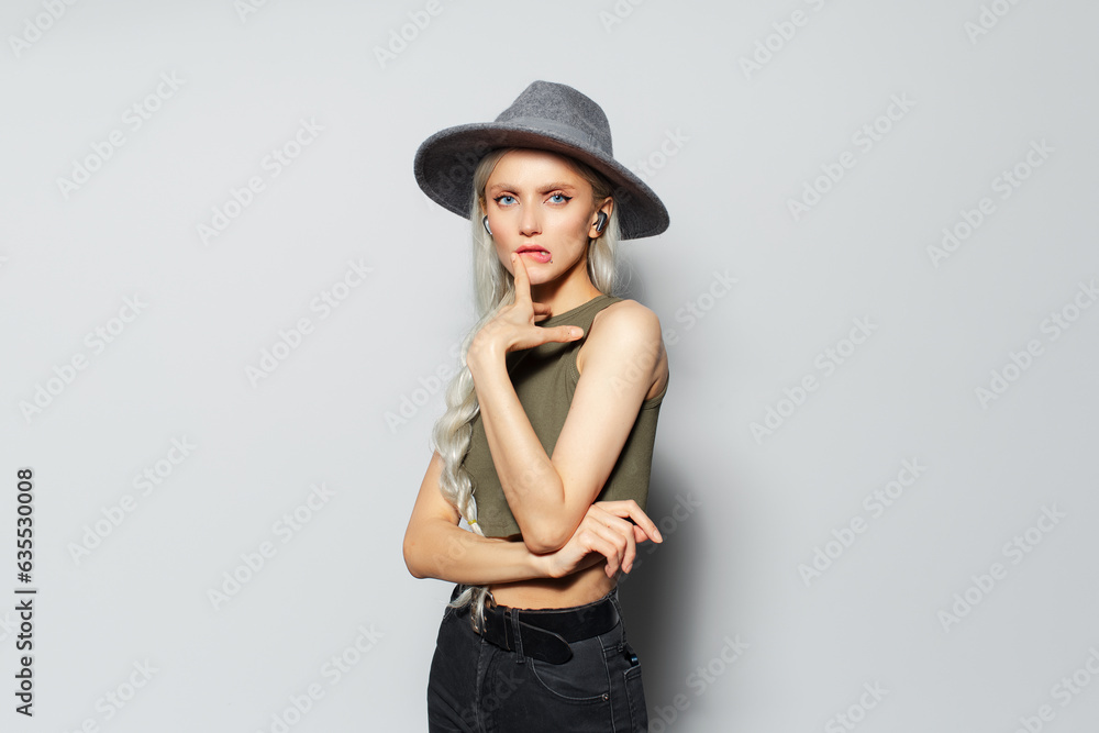 Studio portrait of happy blonde girl with earbuds in ears on white background. Wearing grey hat and green shirt. Studio portrait of happy blonde girl with earbuds in ears on white background. Wearing grey hat and green shirt.
