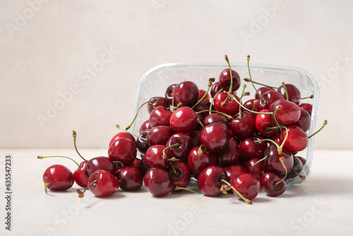 Plastic container with fresh cherry on light background, closeup