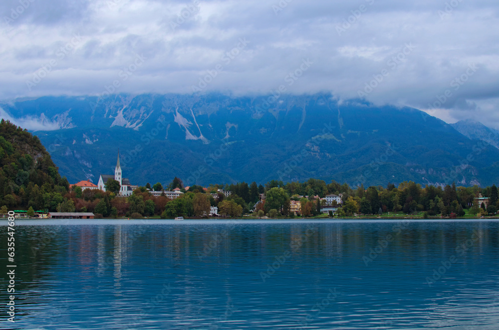 Panoramic landscape view of famous Bled Lake with colorful buildings on lake shore. Beautiful mountains in the background. Cloudy weather. Concept of landscape and nature