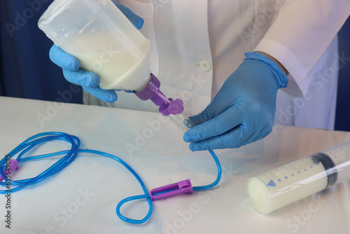 Enteral nutrition diet beeing prepared by a healthcare professional wearing gloves. Professional holding the enteral diet with infusion set connected. Spike connector