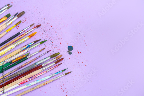 Artist's brushes with paints on lilac background