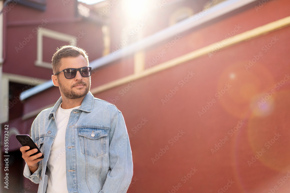 Handsome man wearing denim jacket and sunglasses walking around the city. Handsome man wearing denim jacket and sunglasses walking around the city.