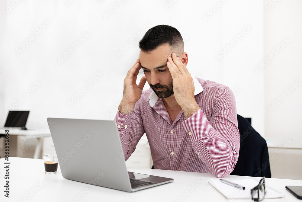 Unhappy tired caucasian mature guy at table with laptop, presses hands to head, suffers from headache, overwork Unhappy tired caucasian mature guy at table with laptop, presses hands to head, suffers from headache, overwork
