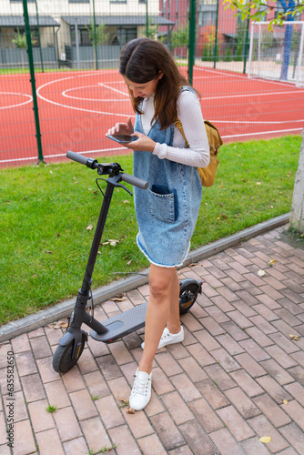 The girl activates the rental of an electric scooter through the application. A tourist girl is going to use an electric scooter through a mobile application on her phone and remotely activate it.