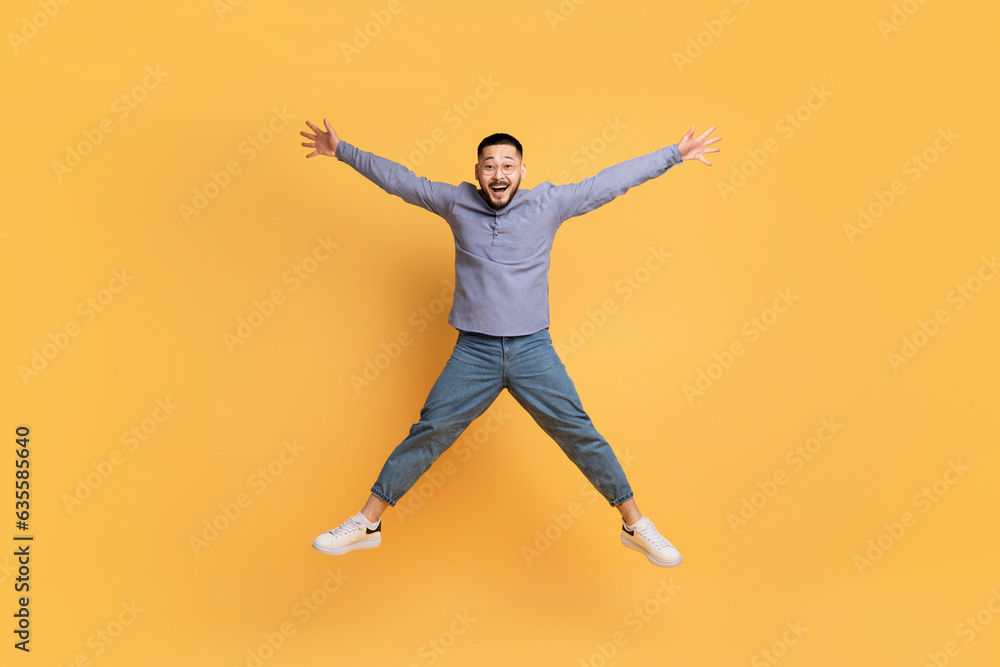 Crazy Sales. Funny Asian Man Jumping Like A Star Over Yellow Background