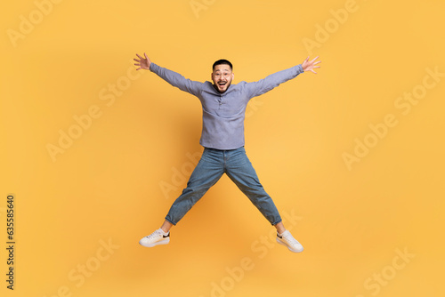 Crazy Sales. Funny Asian Man Jumping Like A Star Over Yellow Background