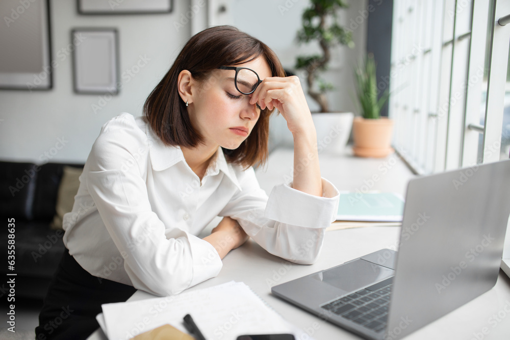 Eyes strain. Overworked businesswoman tired after using laptop, sitting in office, upset woman rubbing nose bridge