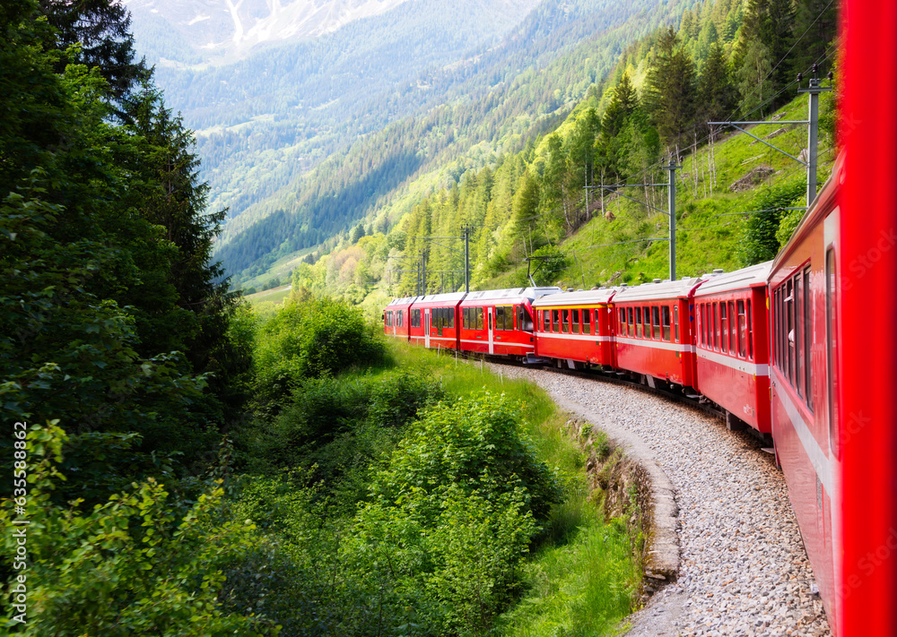 Red train moving in beautiful green summer forest in Switzerland