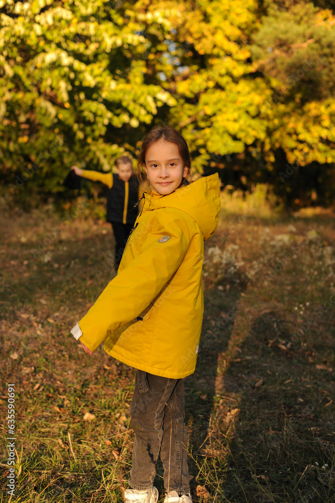 The cute caucasian girl is gluing in the late autumn in the forest. Looking at the camera, wearing a yellow jacket The cute caucasian girl is gluing in the late autumn in the forest. Looking at the camera, wearing a yellow jacket