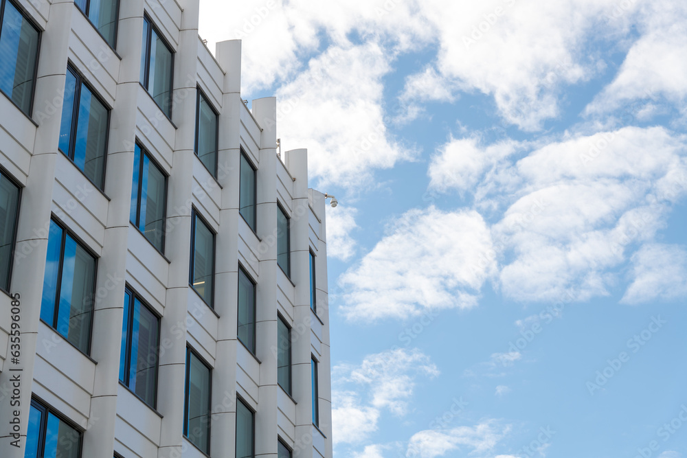 Low angle view of white building corner against blue sky with some clouds. Office or apartment building exterior. Copy space for your text. Urban architecture theme.