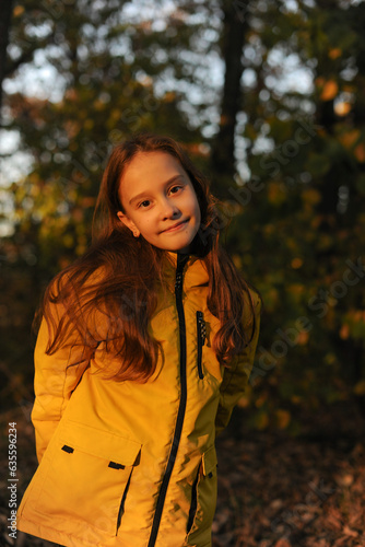 A beautiful caucasian girl dressed in a yellow jacket and with loose hair walks in the forest in late autumn smiling and looks ahead