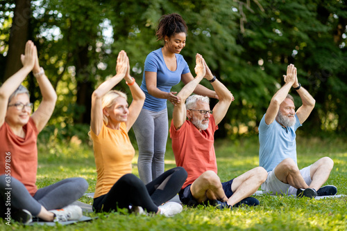 Group of active senior people attending outdoor yoga class with instructor