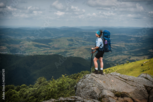 Girl hiker with a backpack stands on a rock in the mountains. Trekking life. Hike through the Carpathian mountains. Green mountain slopes